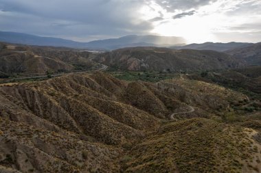 İspanya 'nın güneyindeki dağlık arazi, dağların çalı bitkileri, ağaçlı bir vadi var, gökyüzü bulutlu.