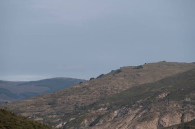 İspanya 'nın güneyindeki Granada dağları, dağların birkaç vadisi var, çalıların ve ağaçların bitkileri var, gökyüzü bulutlu.