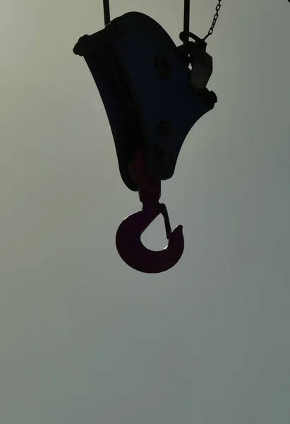 A silhouetted hanging heavy duty harbor crane hook anticipating a pick-up