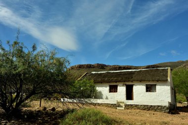 Wupperthal 'ın kırsal bir köyünde eski bir sazdan çatı evi. Arkasında engebeli Cederberg dağları ve bulutlu manzarası var..