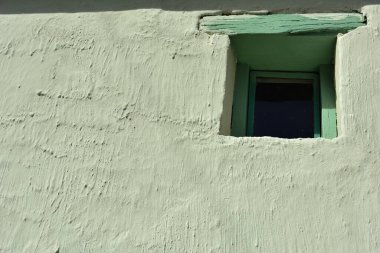 Kalın, beyaz bir duvarda küçük yeşil bir boya ve eski bir pencere.