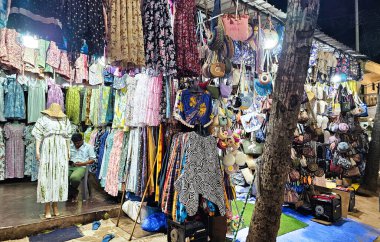 Renkli kıyafetler, çantalar ve aksesuarlar da dahil olmak üzere çok çeşitli ürünleri açık hava ortamında parlak ışıklandırmalı bir ortamda sergiliyor..