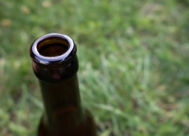 Kahverengi cam bir şişenin boynu yeşil çimenlere karşı
