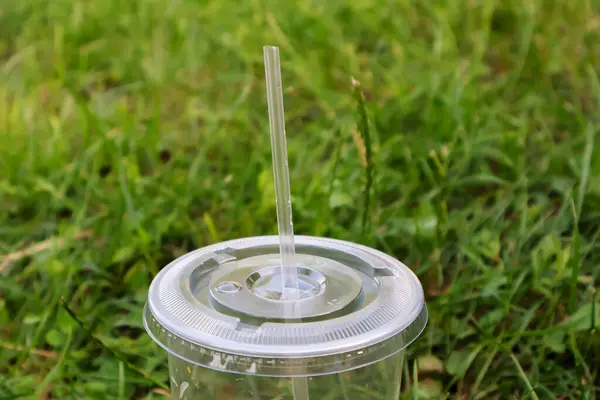 stock image A plastic cup with a lid and a tube on a background of green lawn grass