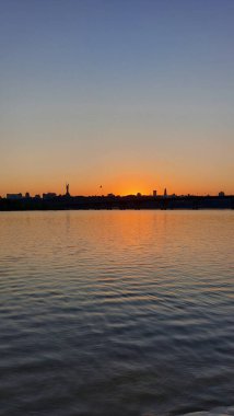 Sunset Over River with Silhouetted Cityscape and Monument clipart