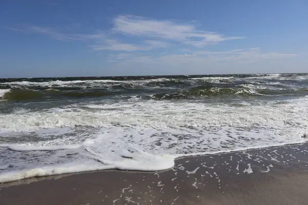 Okyanus Dalgaları mavi gökyüzü altında Sandy Shore 'a çarpıyor: Beyaz köpüklü okyanus dalgalarının açık mavi gökyüzünün altındaki kumlu bir sahile yuvarlanışının manzaralı bir görüntüsü. Doğa, dinginlik ve kıyı manzaraları için mükemmel bir tema..