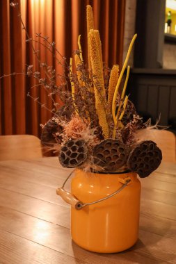 Nilüfer tohumları, otlar ve toprak dokuların bulunduğu, ahşap bir masanın üzerinde canlı, sarı bir metal vazoda sergilenen büyüleyici bir çiçek düzenlemesi..