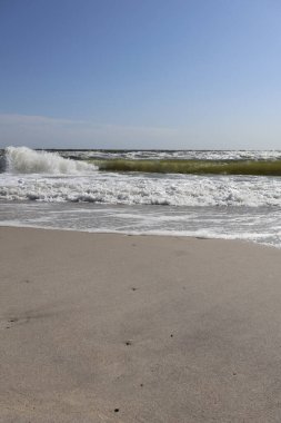 Breaking waves crash onto the sandy shore under a bright blue sky, with the ocean stretching into the distance, capturing the beauty of the coast and natural seascape. clipart