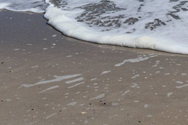 Close-up view of foamy sea waves reaching a sandy shoreline, capturing the peaceful interaction of water and sand. clipart