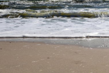 A scenic close-up of ocean waves rolling onto the sandy beach with white foam and clear water patterns clipart