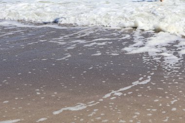 Yumuşak Dalgalar ve Kumsalda Deniz Köpüğü. Yumuşak deniz köpüğünden ve dalgalı dalgalardan oluşan sakin bir yakın çekim. Güneş ışığı altında kumlu sahile çarpıyor..