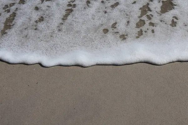 Sandy Shore 'da Ocean Foam' ın yakın çekimi. Yumuşak deniz köpüğü pürüzsüz bir kumsal boyunca uzanır ve okyanusun basitliğini ve güzelliğini yakalar..