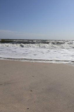 Huzurlu okyanus dalgaları açık mavi bir gökyüzünün altındaki kumlu bir plaja nazikçe yuvarlanıyor. Bu sakin kıyı manzarası rahatlama, seyahat ve doğal güzellik temaları için idealdir..