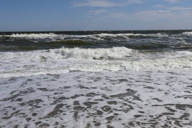 Karadeniz 'in dalgaları Ukrayna' nın kumlu kıyılarına vuruyor güneşli mavi gökyüzünün altında. Köpüklü sörf ve dalgalı su dinamik ve canlı bir deniz manzarası yaratır..
