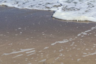 Kumlu kıyı şeridine yayılan yumuşak deniz köpüğünün yakın çekim görüntüsü hassas desenler ve su ile kum arasında sakin bir etkileşim yaratıyor. Sahne, karaya vuran okyanus dalgalarının kısacık güzelliğini yakalar..