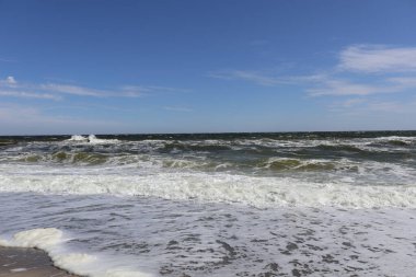 Açık Mavi Gök Altında Güneşli Sahil Dalgaları. Açık, parlak, mavi gökyüzü ile güneşli bir günde, kumlu kıyı şeridinde dalgaların geniş görünümü.