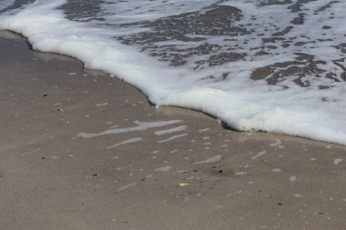 Dalga köpüğü Sandy Shoreline 'a ulaşıyor. Sahil şeridinin dingin ve doğal güzelliğini ön plana çıkaran, kumlu kumsala rastladıklarında köpük oluşturan yumuşak okyanus dalgalarının yakın çekimi..