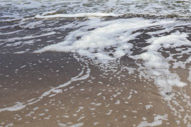 Islak Kum 'da Deniz Köpüğü desenleri. Köpüklü deniz köpüğünün yakın çekimi ıslak kumlu sahilde karmaşık desenler oluşturarak doğanın sanatsal çalışmalarının dinamik güzelliğini yakalıyor..