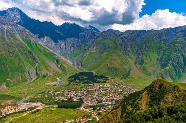Stepantsminda, Saint Stepan, Kazak Dağı eteklerinde bulunan bir köydür. Dağ sırası. Mavi gökyüzü beyaz bulutlarda..