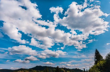 Karpatların üzerinde beyaz bulutlar olan mavi gökyüzü. Kabarık beyaz bulutlu parlak mavi gökyüzünün yatay görüntüsü. Uzayı kopyala..