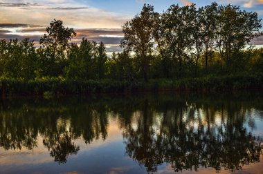 Gün batımı, gün doğumu, yaz manzarası. Güzel bir doğa. Bulutlar ve ağaçlar nehre yansıyor. Sanatsal duvar kağıdı. Çok canlı bir atmosfer..