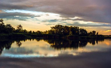 Nehrin üzerinde yaz günbatımı. Bulutlar ve ağaçlar nehre yansıyor. Sanatsal duvar kağıdı. Çok canlı bir atmosfer..