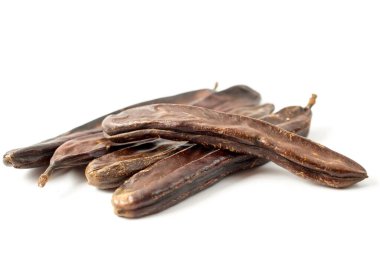 Kurumuş keçiboynuzu tohumlarıyla dolu bir grup beyaz arka planda izole edilmiş.