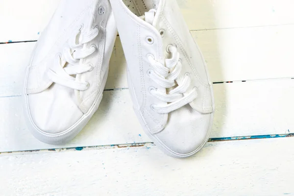 Youth white sneakers with white untied the laces on wooden background