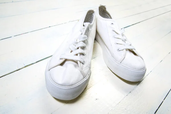 Youth white sneakers with white untied the laces on wooden background