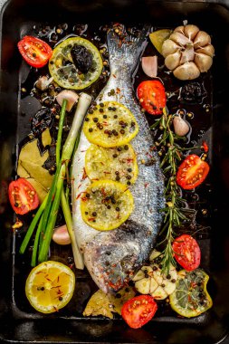 Lezzetli taze çipura ya da koyu arkaplanda dorade balığı. Aromatik otlu balık, limon, sarımsak, baharat ve sebzeler - sağlıklı yiyecek, diyet veya pişirme konsepti