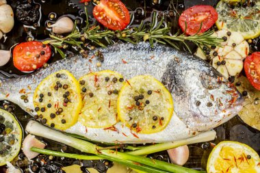 Lezzetli taze çipura ya da koyu arkaplanda dorade balığı. Aromatik otlu balık, limon, sarımsak, baharat ve sebzeler - sağlıklı yiyecek, diyet veya pişirme konsepti