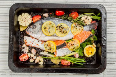 Koyu arkaplanda taze çipura ve somon balığı. Aromatik otlu, baharatlı ve sebzeli balıklar - sağlıklı yiyecekler, diyet veya yemek pişirme konsepti