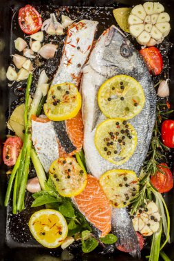 Koyu arkaplanda taze çipura ve somon balığı. Aromatik otlu, baharatlı ve sebzeli balıklar - sağlıklı yiyecekler, diyet veya yemek pişirme konsepti