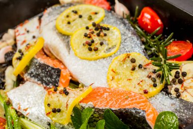 Koyu arkaplanda taze çipura ve somon balığı. Aromatik otlu, baharatlı ve sebzeli balıklar - sağlıklı yiyecekler, diyet veya yemek pişirme konsepti