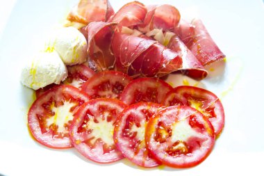 Jambon karışımı. Jambon. Geleneksel İtalyan ve İspanyol tuzlama, sigara içme, kurutulmuş yemek - jamon Serrano ve krema ve domatesle dilimlenmiş jambon kabuğu