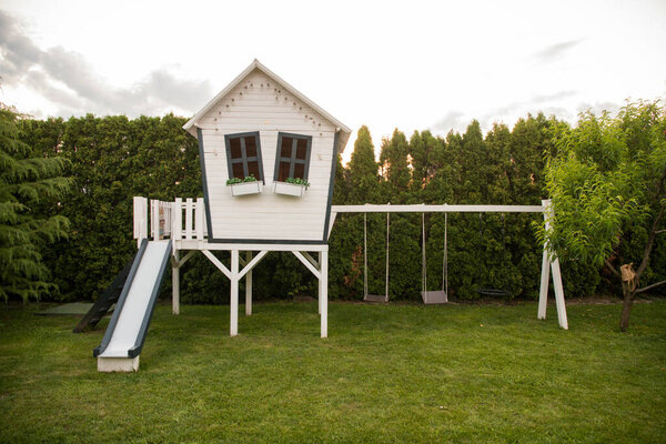 White wooden children's house with slide and swing