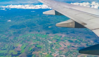 Aşağıdaki dünyaya bir uçak penceresinden bakan manzaralı hava manzarası. Yumuşak bulutları olan güzel, açık mavi bir gökyüzü. Seyahat kavramı