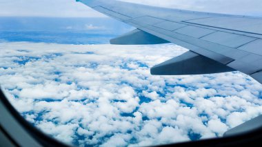 Pofuduk bulutların uçağın penceresinden uçtuğu güzel, berrak mavi gökyüzü manzarası, canlı doğal manzara. Seyahat konsepti, gezgin, gezi, tatil, turizm, manzara, arka plan