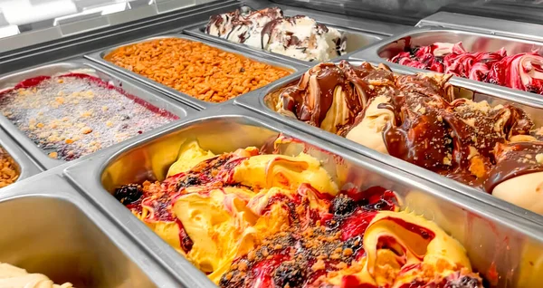 Colorful Italian ice cream with various fruit flavors decorated with fruits, nuts or chocolate  in the refrigerator-display case. Ice cream trays. Italian cuisine. Gourmet dessert.