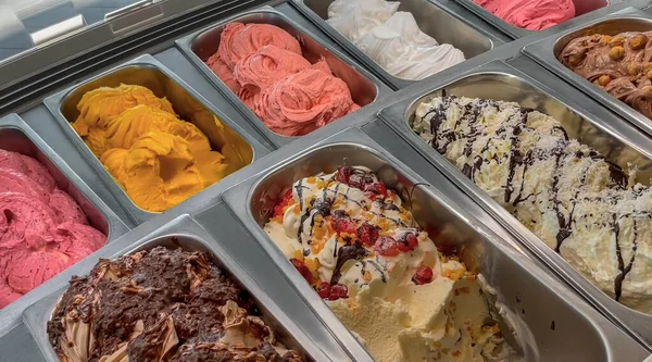 Colorful Italian ice cream with various fruit flavors decorated with fruits, nuts or chocolate  in the refrigerator-display case. Ice cream trays. Italian cuisine. Gourmet dessert.
