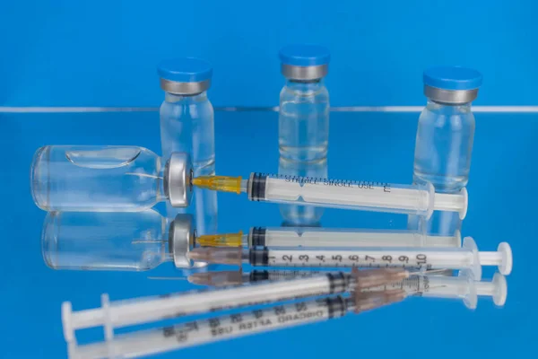 Injection ampoules with syringes and needles ready for use. Isolated on a blue background. Close-up. Interior. Macro. Selective focus. Sterilized medical equipment. Medical concept.