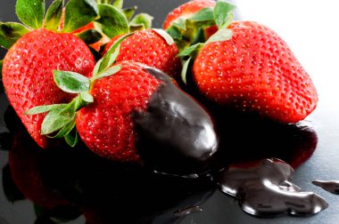 Strawberries dip in sweet chocolate sauce with black background.