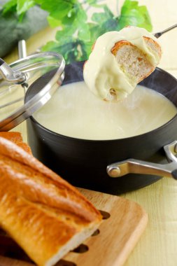 Gourmet swiss fondue dinner on a winter evening with pot of cheese fondue and forks dipping bread.