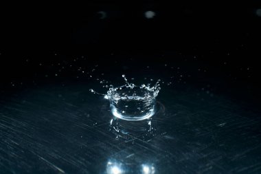 Koyu bir arka plan dalgası üzerine su damlatan makro damlalar mavi bir ışık yansıması