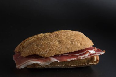 Mutlak siyaha izole edilmiş jambonlu bir sandviçin yaşamı yemeğin dokusunu yükseltiyor.