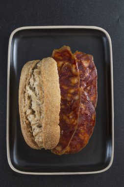 Sade bir kompozisyon ve siyah arkaplan içinde koyu renkli bir tepsiye yerleştirilmiş bir sucuklu sandviçin görüntüsü