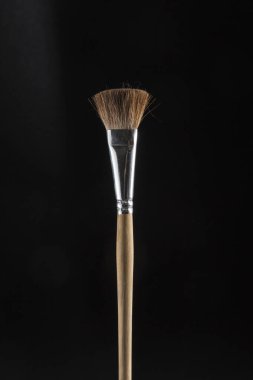 Genişletilmiş kahverengi tüyleri olan ahşap boya fırçası, siyah bir arkaplana yerleştirilmiş, stilize bir figürü vurguluyor.