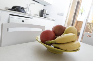 Muzlu meyve kasesi ve domatesler, beyaz bir mutfağın masasına, modern ve güncel bir tarzla yerleştirildi.