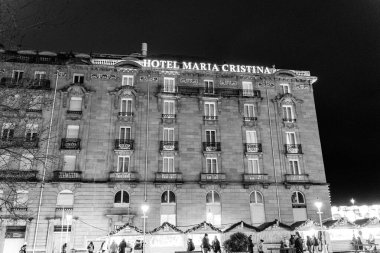 Yıldızlı bir gökyüzünün altında, büyük bir otel dekoratif mimarisi ile gurur duyar ve gece şehrin cazibesini yansıtır. Neşeli ışıklar ve neşeli ziyaretçiler çevreyi canlandırıyor. Maria Cristina Oteli. San Sebastian, İspanya.