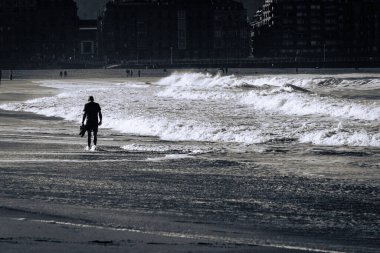 Alacakaranlık çöktüğünde, kumlu sahilde tek başına gezinen, dalgaların ritmini hisseden ve okyanus esintisini tazeleyen biri. Çevre sakin bir kıyı manzarasına karışıyor. San Sebastian, İspanya, Bask Ülkesi..